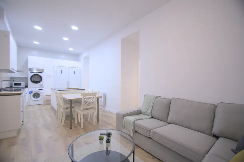 Salón con sofá y cocina abierta, amueblados y equipados por eldormitorio