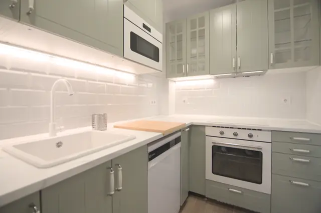 Cocina con muebles verde salvia, encimera blanca y horno