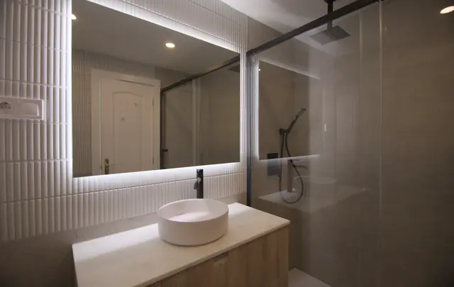 Baño con lavabo de sobre encimera, espejo retroiluminado y ducha