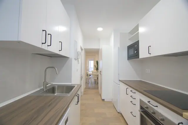 Cocina blanca en paralelo con encimera de madera, horno y microondas